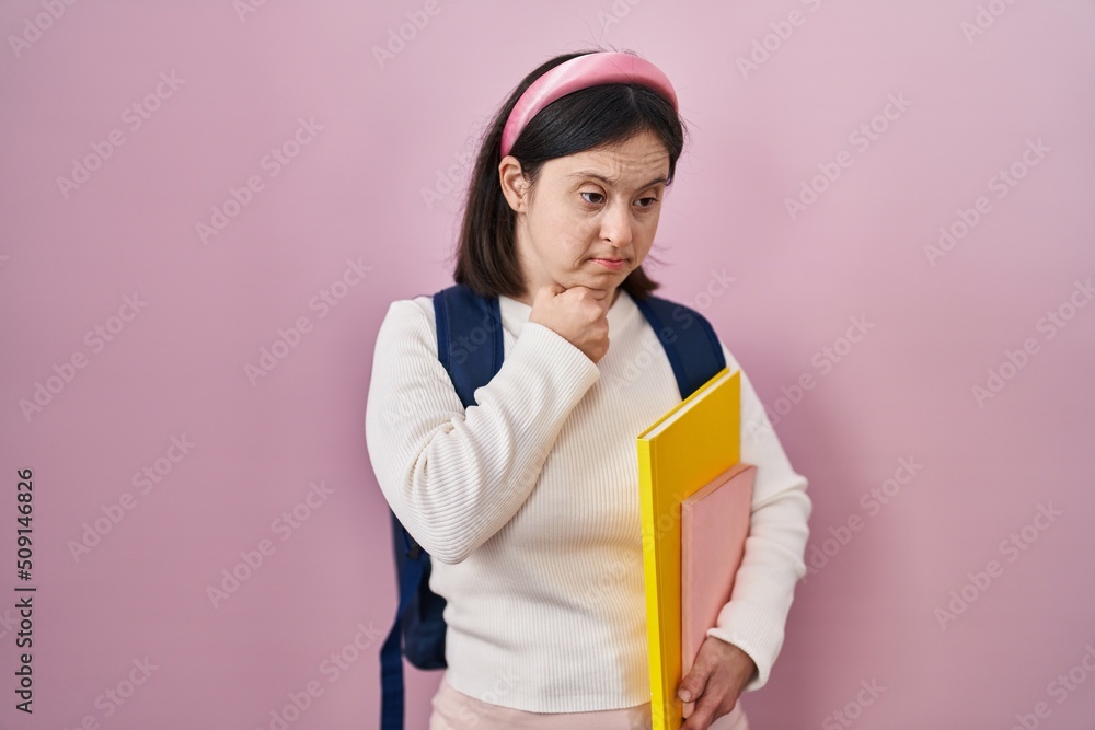 Wall mural Woman with down syndrome wearing student backpack and holding books looking confident at the camera smiling with crossed arms and hand raised on chin. thinking positive.