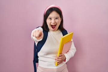 Woman with down syndrome wearing student backpack and holding books pointing displeased and...