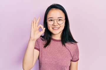 Young chinese girl wearing casual clothes and glasses smiling positive doing ok sign with hand and fingers. successful expression.