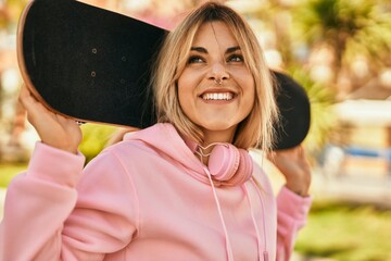 Young blonde skater girl smiling happy holding skate at the city. © Krakenimages.com