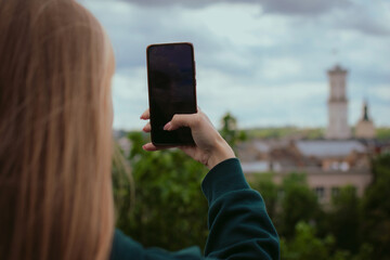 Closeup woman’s hand holding mobile phone taking photos of an old city in Europe. Female tourist or blogger enjoying trip. Travel and sightseeing concept