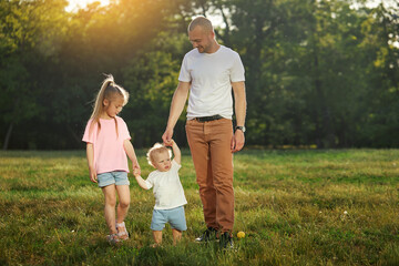 Fototapeta premium A young father of two children. Happy parenting. Dad spends happy time with his cute kids in the park