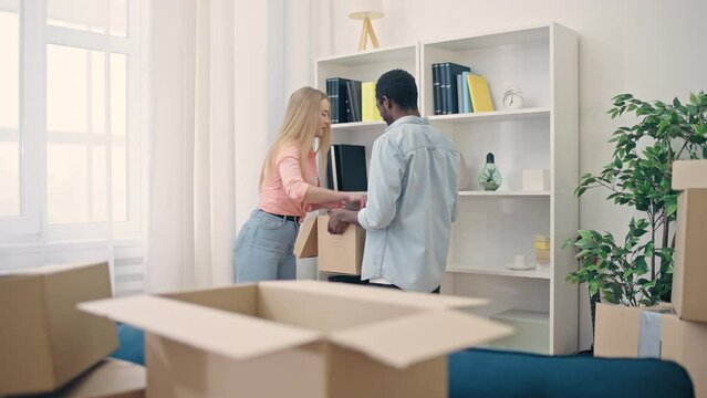 Multiethnic happy couple packing books in box and smiling, moving out together