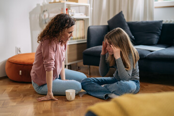 mother comforts her depressed teenager daughter in living room