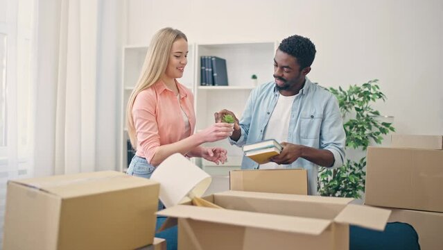 Biracial couple packing belongings in box and smiling, happy to buy new home