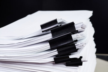 A stack of office papers, some of which are fastened with black binders