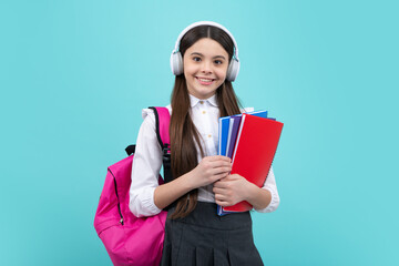 Schoolgirl, teenage student lifestyle girl in headphones hold books on blue isolated studio background. School and music education concept.