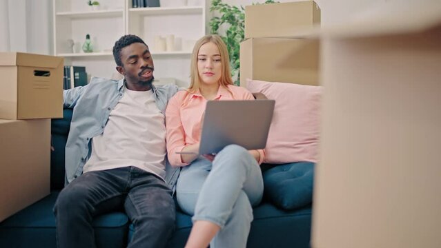 Multiethnic couple with laptop choosing furniture for new home, cleaning service