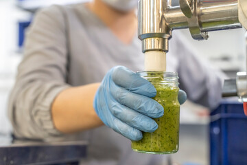 Pesto sauce Industrial process. High quality sauce production. Worker operator at the food factory behind the machine pours pesto sauce into jars. Italian basil taste in Pesto sauce