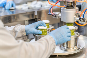 Pesto sauce with basil Industrial process. Factory worker working on vacuum sealing machine for canned food. production of Pesto sauce. Vacuum Seamer for Cylindrical Cans of Rotary Type