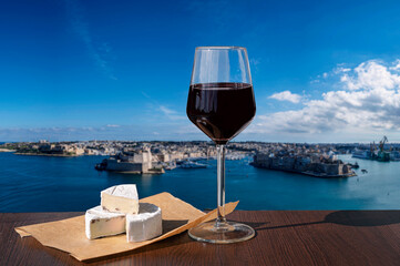 Glass of red wine with cheese with view of city wall and harbor in Valletta, Malta.