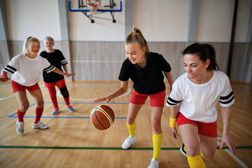 Young and senior women playing basketball match in gym.