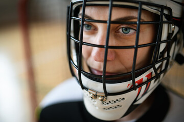 Close-up of woman floorball goalkeeper in helmet concetrating on game in gym.