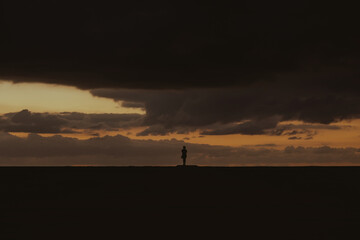 Naklejka na ściany i meble silhouette of a female traveler in a beautiful cloudy sunset on the beach, at the golden hour