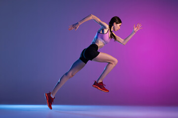Fototapeta na wymiar One young muscular girl, female runner or jogger training isolated on pink-blue background in neon light. Sport, track-and-field athletics, competition and active lifestyle concept