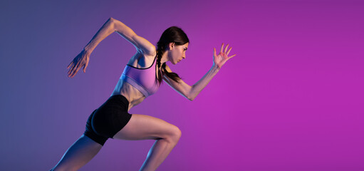 One young muscular girl, female runner or jogger training isolated on pink-blue background in neon light. Sport, track-and-field athletics, competition and active lifestyle concept