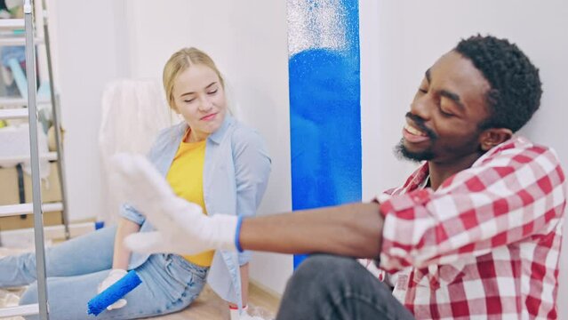 Happy interracial couple with paint rollers taking a break from work and talking