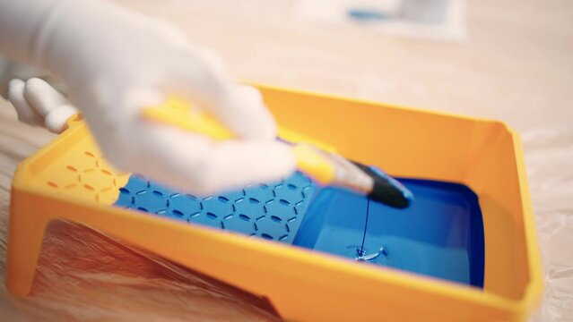 Person dipping brush into blue paint in tray, slow-motion, home repair service
