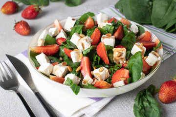 Healthy salad with strawberries, spinach, feta and pine nuts dressed with balsamic in plate on light gray background