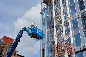 Fototapeta na wymiar Construction of a multi-storey building. Finishing of the façade with glass panels. Tower crane.
