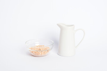 Jug of non dairy oat milk and oat flakes in glass bowl on white background. Healthy vegan food concept