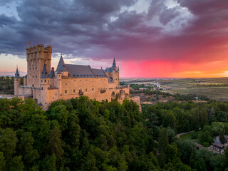 Fototapeta premium Sunset over the Alcázar of Segovia medieval castle in Castile and León, Spain. Rising out on a rocky crag above the confluence of two rivers with majestic red, orange, yellow as the sun paints the sky