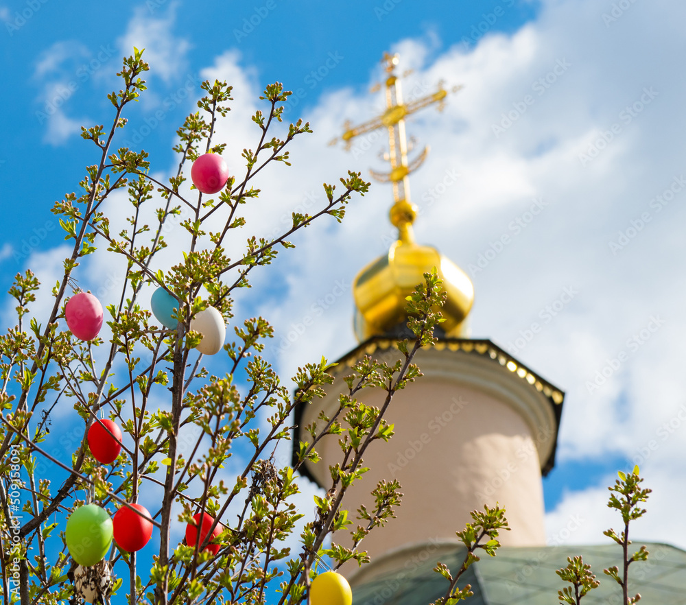 Wall mural Colorful easter eggs on the tree near the church in sunny spring 