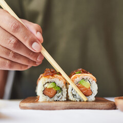 Comiendo con palillos aburi uramaki. Sushi roll de salmón y aguacate con cebolla caramelizada.