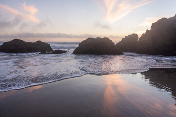 Receding ocean tides at Pfeiffer beach leaves a layer of water reflecting the sunset clouds.