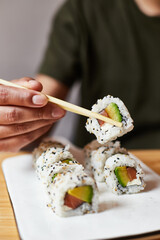 Comiendo uramaki de salmón, queso crema y aguacate en casa. Domicilio de restaurante japonés. Cogiendo con palillos sushi 