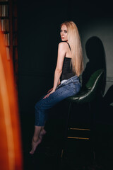 Fototapeta na wymiar A model-looking girl sits sideways in a chair with blond hair in a hard light.