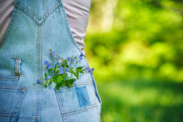 Woman in denim jumpsuit with field flowers in her back pocket. Summer vacation concept. Copy space.
