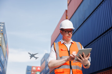 the logistic business owner is wearing a white safety helmet and using the digital tablet in a...