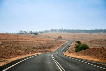 Fototapeta na wymiar Winding open empty road surrounded by farms and fields in Australia. Road trip travel
