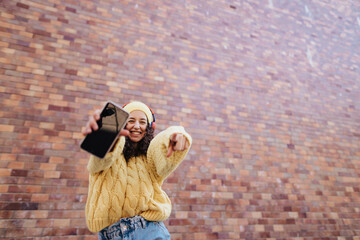 Portrait of happy young woman in front of brick wall in city street, looking at camera.