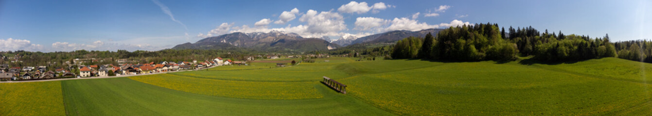 Panorama of beautiful european countryside with green field forest mountains houses and clouds at springtime.