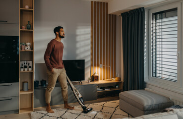 Young man vacuum cleaning carpet in living room