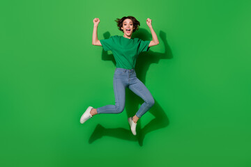 Fototapeta na wymiar Full body portrait of delighted satisfied girl jumping raise fists shout yes isolated on green color background