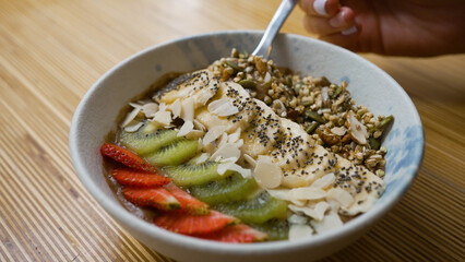 Vegan bowl with banana kiwi and strawberry on wooden table. Cocoa yogurt taken by tablespoon. Vegan bowl with fruits and seeds for breakfast closeup