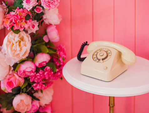 retro rotary telephone standing on a table in a pink room next to flowers