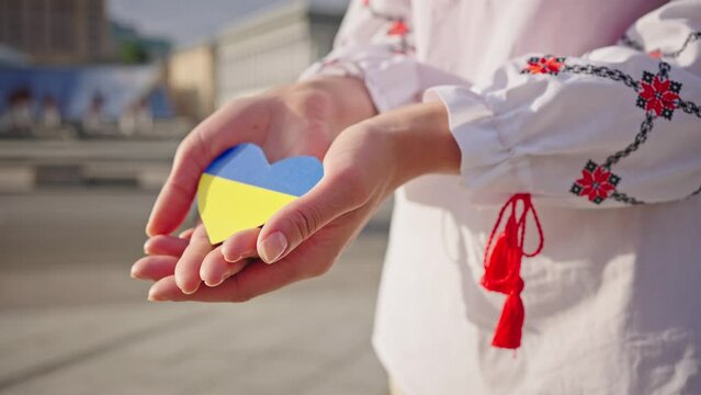 Woman hands hold paper heart painted in Ukraine flag colors