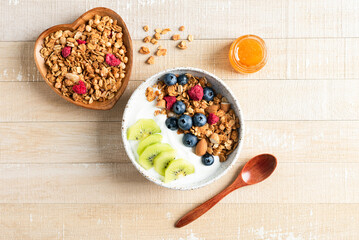 Bowl of crunchy honey granola with blueberries, kiwi and greek yogurt on a wooden background. Top view