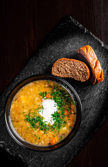 Soup with meat, pickled cucumbers and pearl barley in black bowl on black wooden table background