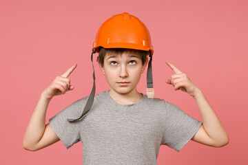 the boy points his finger at the orange helmet on his head, pink background