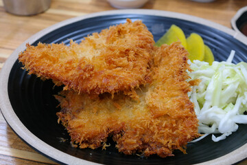 Crispy pork cutlet and salad are served on a round plate.