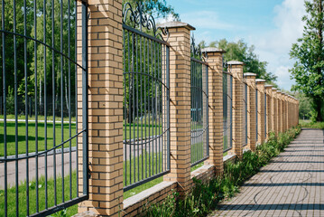 Fence with wrought iron lattice and brick pillars outdoors on sunny summer day, side view