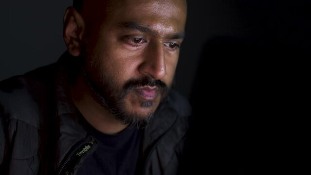 Ethnic Minority Male Intently Viewing Laptop  In The Dark. Viewed Behind Monitor. Locked Off