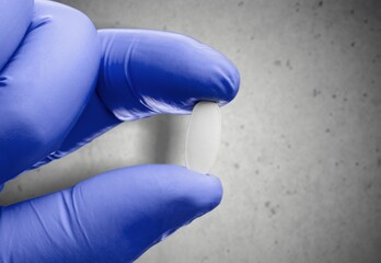 Hand with blue glove showing a probiotic or medication capsule pill