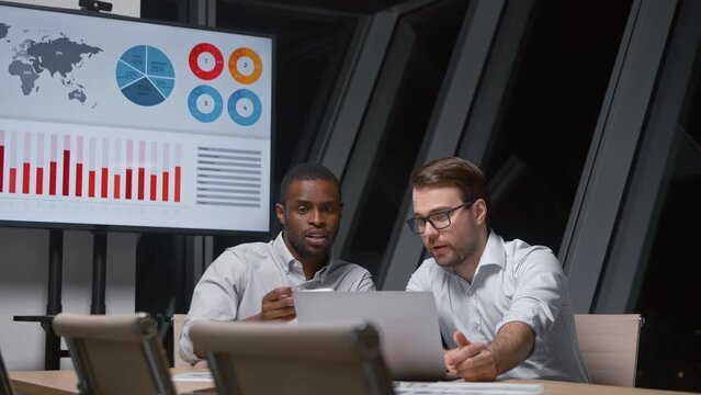 Two diverse business men discussing financial market data using laptop