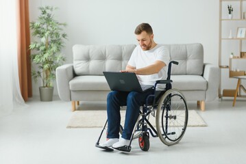 Work at home. Paralyzed male person holding laptop on knees and keeping smile on face while looking at screen.